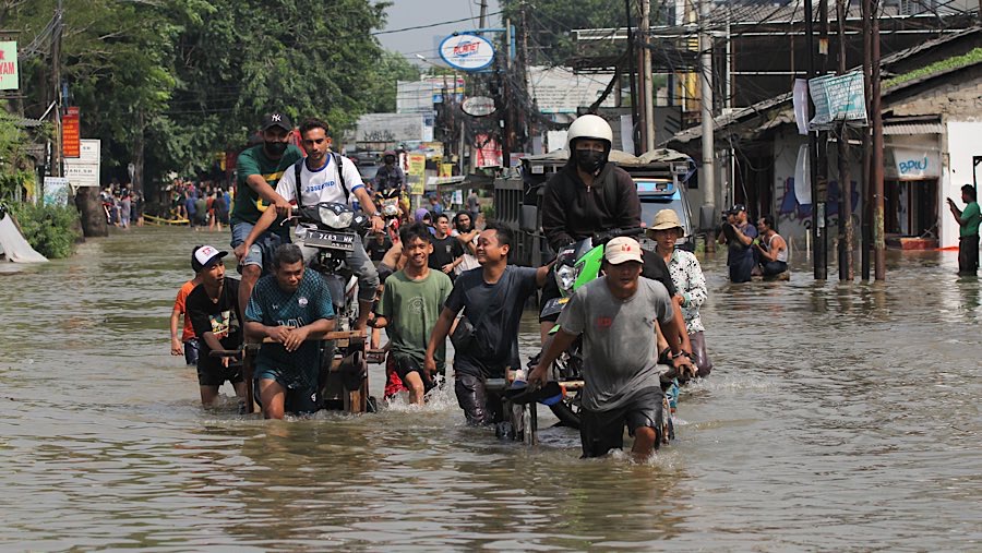 Beberapa pengendara motor terlihat memanfaatkan ojek gerobak untuk melewati genangan air. (Bloomberg Technoz/Andrean Kristianto)