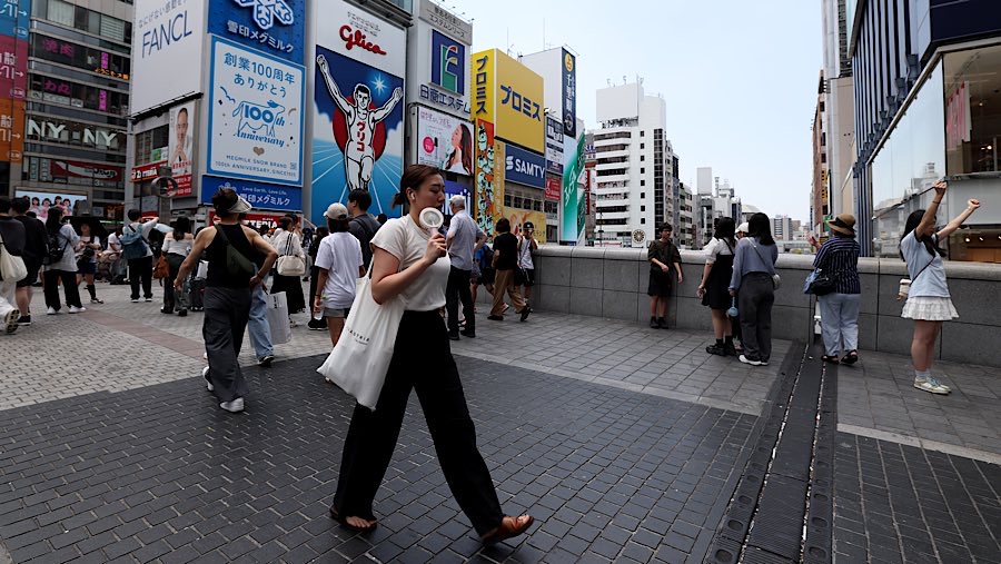 Pejalan kaki membawa kipas angin genggam saat suhu tinggi di Dotonbori, Osaka, Jepang, Kamis (31/7/2025). (Buddhika Weerasinghe/Bloomberg)