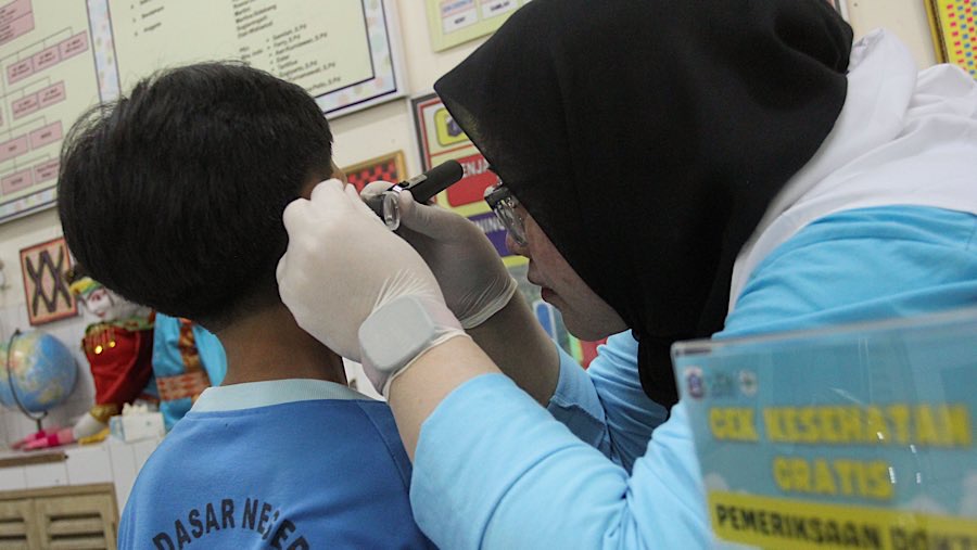 Petugas Puskesmas terlihat dengan teliti memeriksa kuping para siswa. (Bloomberg Technoz/Andrean Kristianto)