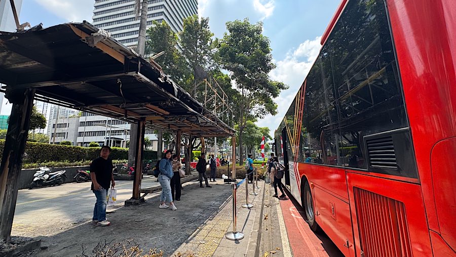 Penunpang menunggu bus di halte Ratu Plaza yang rusak akibat demo di Jend. Sudirman, Senin (1/9/2025). (Bloomberg Technoz/Andrean Kristianto)