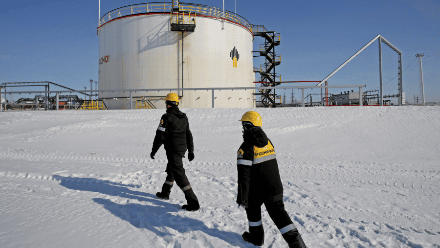 Pekerja berjalan melewati tangki penyimpanan minyak di stasiun pompa, yang dioperasikan oleh Rosneft PJSC, di ladang minyak Samotlor, Rusia./Bloomberg