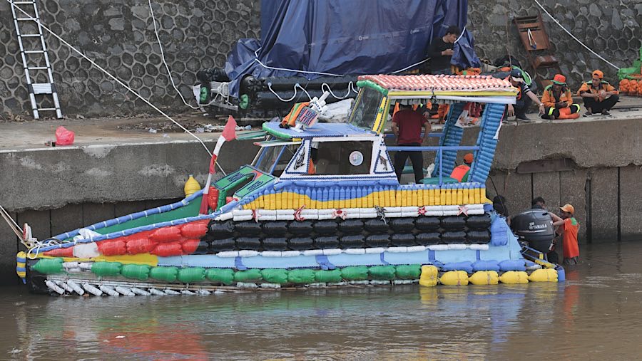 Petugas UPS Badan Air menurunkan perahu dari limbah botol di Kali Ciliwung, Cikoko, Jakarta, Selasa (23/9/2025) (Bloomberg Technoz/Andrean Kristianto)