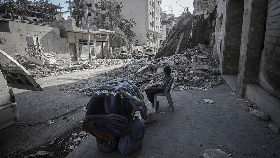 Seorang anak menunggu dengan barang bawaannya di dekat puing-puing bangunan di Kota Gaza, Gaza, Senin (29/9/2025). (Ahmad Salem/Bloomberg)