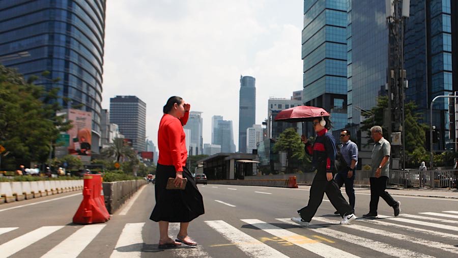 Warga berjalan sambil memakai payung saat cuaca panas di Jalan Jend Sudirman, Jakarta, Selasa (14/10/2025). (Bloomberg Technoz/Andrean Kristianto)