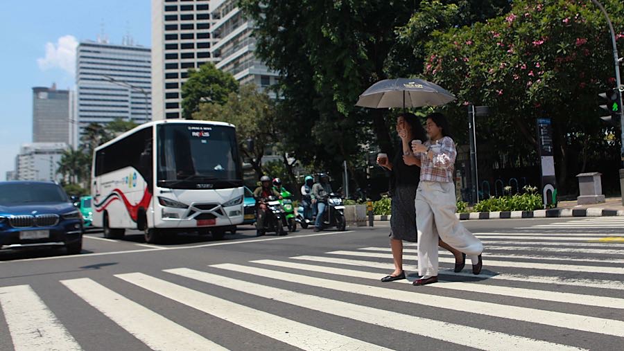 Warga berjalan sambil memakai payung saat cuaca panas di Jalan Jend Sudirman, Jakarta, Selasa (14/10/2025). (Bloomberg Technoz/Andrean Kristianto)