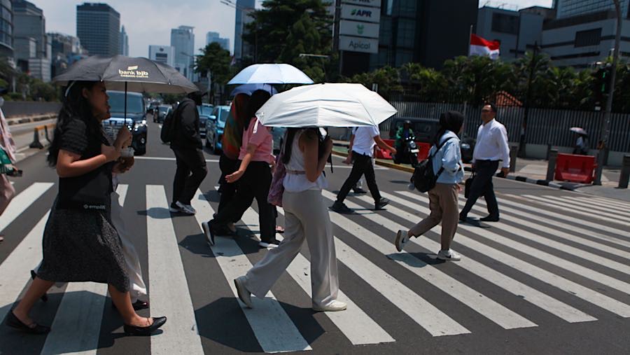 Warga berjalan sambil memakai payung saat cuaca panas di Jalan Jend Sudirman, Jakarta, Selasa (14/10/2025). (Bloomberg Technoz/Andrean Kristianto)