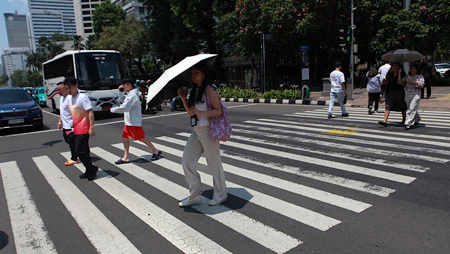 Warga berjalan sambil menggunakan payung saat cuaca panas di Jalan Jend Sudirman, Jakarta, Selasa (14/10/2025). (Bloomberg Technoz/Andrean Kristianto)