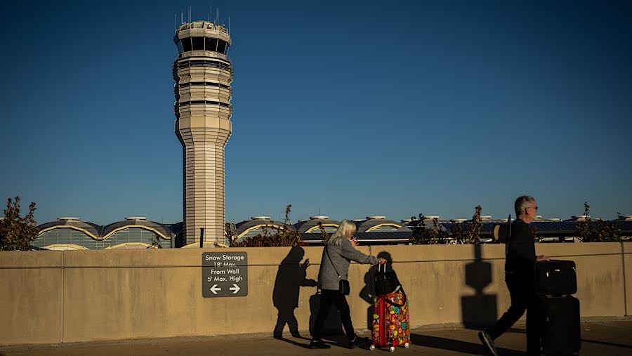 Penumpang melewati menara pengawas lalu lintas udara di Bandara Ronald Reagan Washington di Arlington, AS, Kamis (6/11/2025). (Graeme Sloan/Bloomberg)