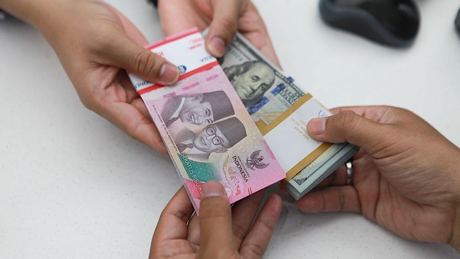 Karyawan memberikan uang rupiah dan dolar AS kepada nasabah di salah satu bank di Jakarta, Senin (1/12/2025). (Bloomberg Technoz/Andrean Kristianto)