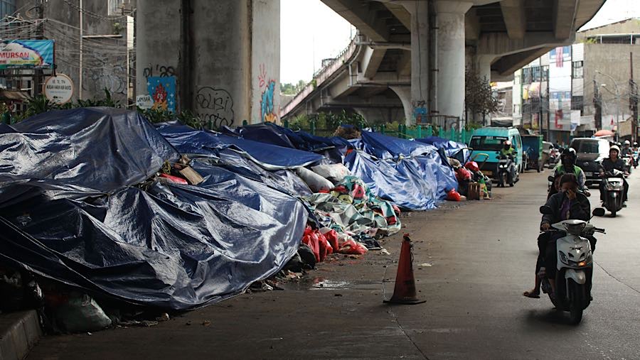 Pengendara motor melintas di samping tumpukan sampah yang ditutupi terpal di Jln. Ir H. Juanda, Tangsel, Rabu (17/12/2025). (Bloomberg Technoz/Andre)