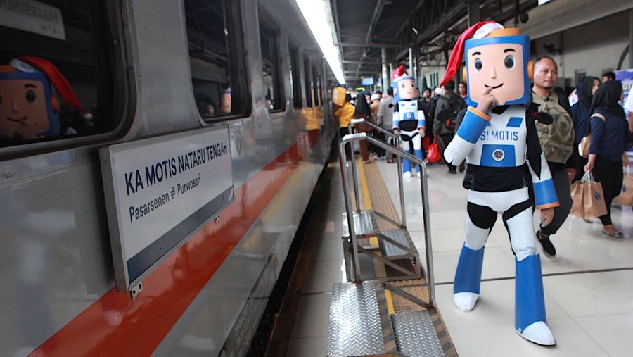 Maskot Si Motis berjalan di samping KA Motis Nataru Tengah di Stasiun Pasar Senen, Selasa (23/12/2025). (Bloomberg Technoz/Andrean Kristianto)