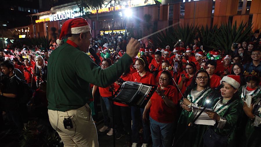 Para penyanyi dipandu seorang dirigen yang berdiri di tengah, mengangkat tangan tinggi untuk mengatur tempo. (Bloomberg Technoz/ Andrean)