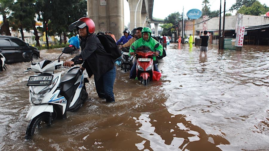 Pengendara menuntun motornya saat melewati banjir di Petukangan, Ciledug Raya, Jumat (20/2/2026). (Bloombeg Technoz/Andrean Kristianto)