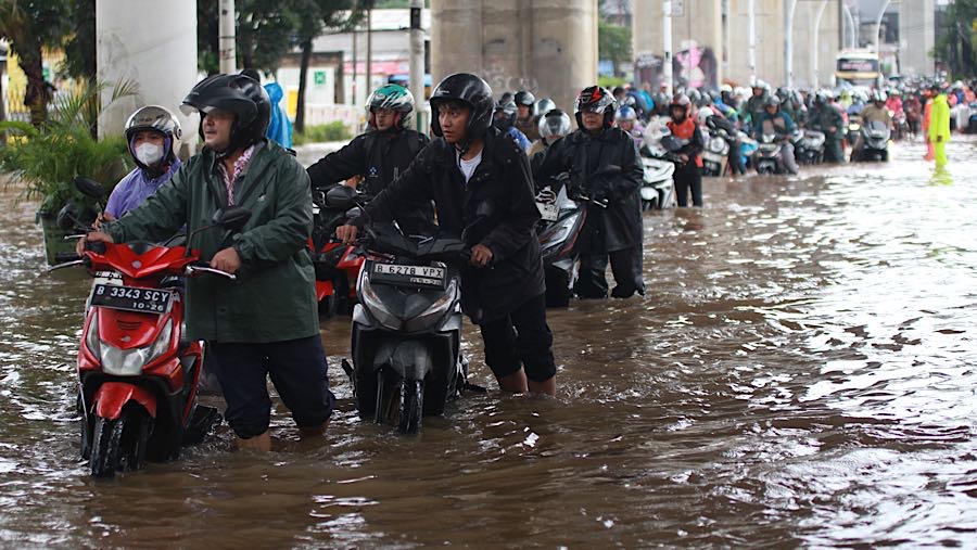 Pengendara menuntun motornya saat melewati banjir di Petukangan, Ciledug Raya, Jumat (20/2/2026). (Bloombeg Technoz/Andrean Kristianto)