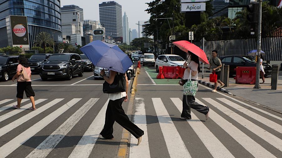 Warga menggunakan payung saat cuaca panas di jalan Sudirman, Jakarta, Kamis (19/3/2026). (Bloomberg Technoz/Andrean Kristianto)