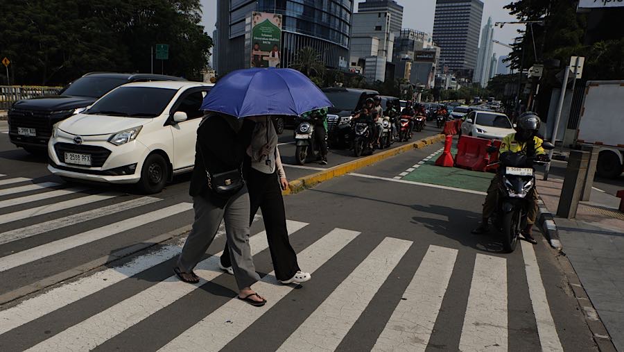 Warga menggunakan payung saat cuaca panas di jalan Jend. Sudirman, Jakarta, Kamis (19/3/2026). (Bloomberg Technoz/Andrean Kristianto)
