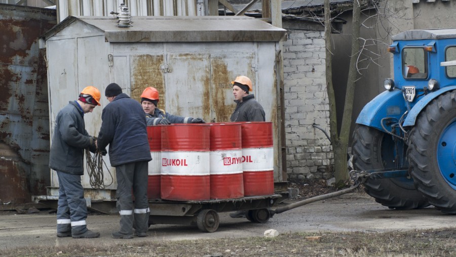 Para karyawan menggunakan traktor untuk memindahkan barel minyak berlogo OAO Lukoil./Bloomberg-Vincent Mundy