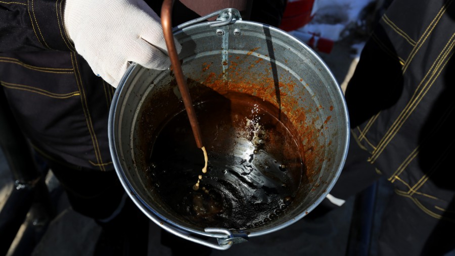 Para pekerja menggunakan ember untuk mengambil sampel minyak mentah di anjungan pengeboran multi-sumur./Bloomberg-Andrey Rudakov