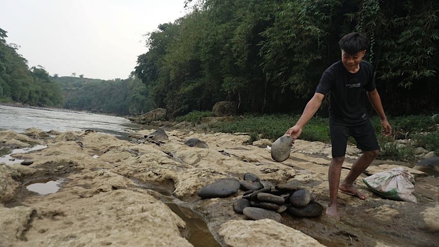 Menyusutnya debit air juga dimanfaatkan warga untuk mengumpulkan batu yang akan digunakan memperbaiki makam. (Bloomberg Technoz/Andrean Kristianto)