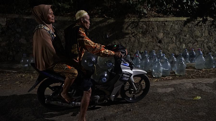 Para suami datang dengan membawa motor lalu membawanya galon itu pulang bersama istri. (Bloomberg Technoz/Andrean Kristianto)