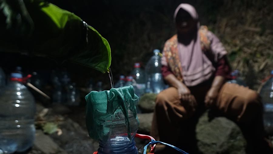 Air yang mengucur dari mata air sangat pelan sehingga warga harus menunggu lama untuk mengisi 1 galon. (Bloomberg Technoz/Andrean Kristianto)