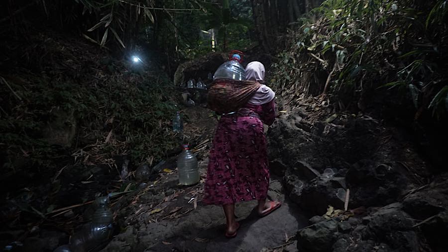 Bagi ibu-ibu yang tidak ditemani oleh suaminya, mereka harus membawa sendiri galon melewati bebatuan licin. (Bloomberg Technoz/Andrean Kristianto)