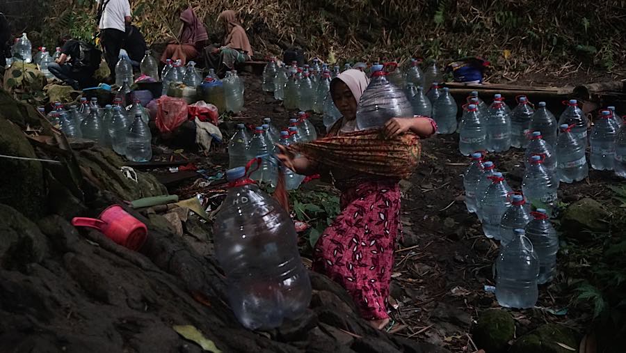 Usai galon terisi para ibu-ibu tersebut lalu menggendong galon itu dan merapihkan menunggu untuk dijemput suami.(Bloomberg Technoz/Andrean Kristianto)