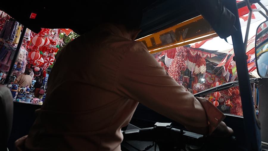 Pengemudi bajaj melintas di depan pernak-pernik kemerdekaan di Pasar Jatinegara, Jakarta, Selasa (11/8/2026). (Bloomberg Technoz/Andrean Kristianto)