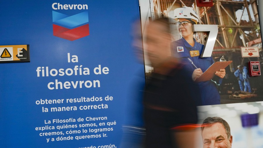 Seorang pekerja melintasi papan nama di kantor Chevron Corp. di Caracas, Venezuela./Bloomberg-Matias Delacroix