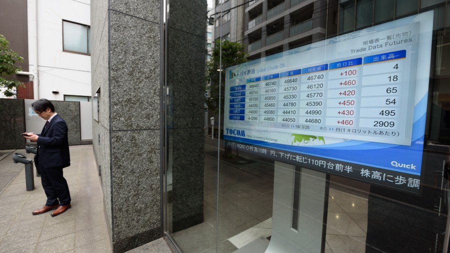 Seorang pria berdiri di dekat layar yang menampilkan harga minyak mentah di Tokyo Commodity Exchange Inc. (Tocom) di Tokyo, Jepang./Bloomberg-Akio Kon