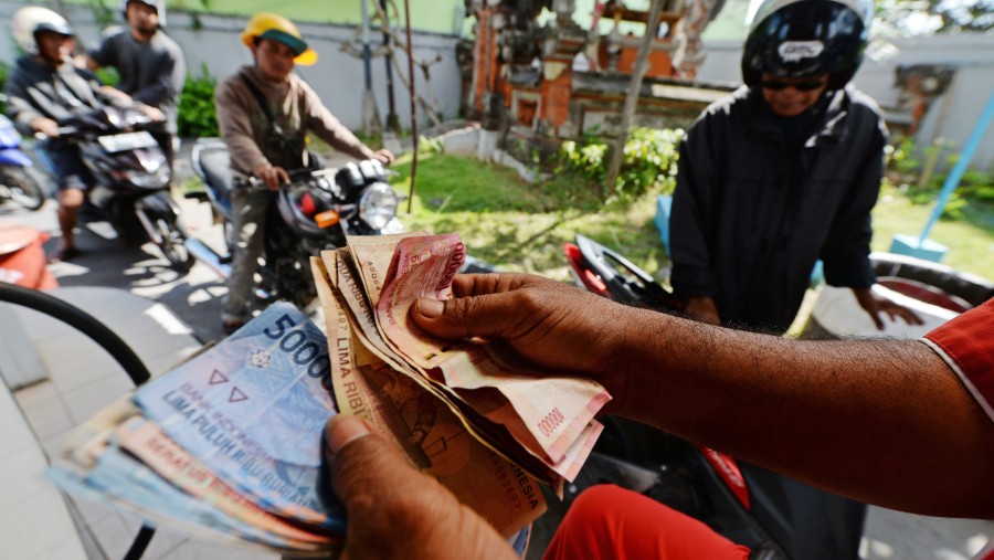 Seorang petugas menghitung uang kertas rupiah sementara para pelanggan mengantre di SPBU Pertamina kawasan Nusa Dua, Bali./Bloomberg-Dimas Ardian