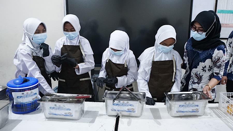 Sebelum pembagian dimulai, siswa yang bertugas piket terlebih dahulu mengenakan celemek, sarung tangan, dan masker. (Bloomberg Technoz/Andrean K)