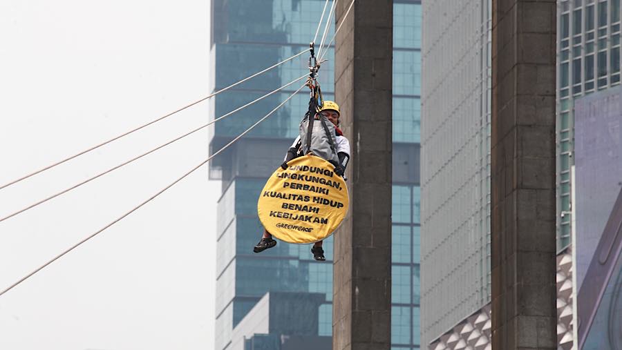 Mereka kemudian turun secara bergiliran menggunakan tali sling tersebut sambil menggenggam poster berbentuk bulat. (Bloomberg Technoz/Andrean K)
