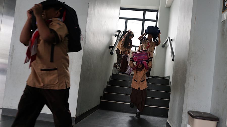 Mereka keluar kelas dan menuruni tangga menuju lapangan sekolah dengan tangan melindungi kepala. (Bloomberg Technoz/Andrean Kristianto)