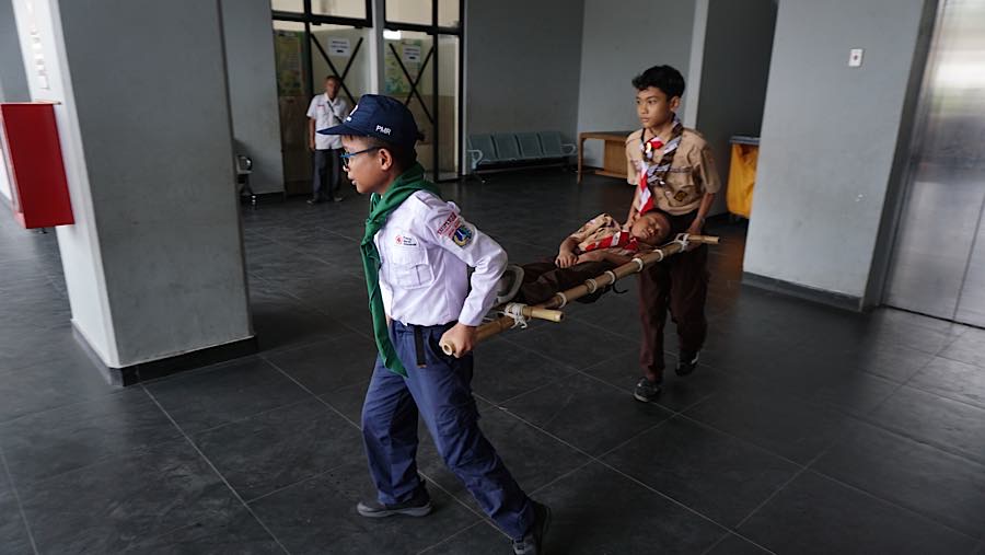 Anggota Palang Merah Remaja (PMR) dan Pramuka turut membantu membawa siswa tersebut menggunakan tandu. (Bloomberg Technoz/Andrean Kristianto)
